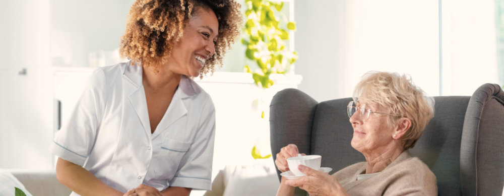 a black caregiver smiling with her elderly female client